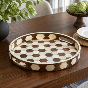 May include: A round serving tray featuring a geometric pattern of alternating dark brown wood and off-white hexagonal tiles. The tray has a raised rim with integrated side handles, showcasing a consistent honeycomb design across the base.