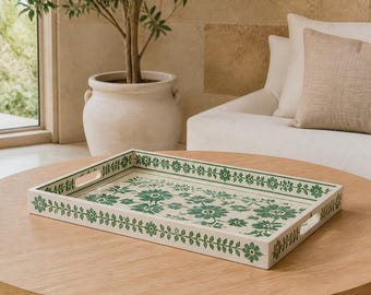 Peut inclure: Un plateau de service rectangulaire avec une base blanche et un motif floral vert. Le design présente un motif de vigne répétitif sur les bords et un arrangement central de diverses fleurs vertes. Le plateau inclut deux poignées latérales.