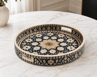 Peut inclure: Un plateau décoratif rond orné d'un motif floral complexe dans des tons bleu marine, crème et doré. Le plateau présente un bord surélevé avec deux poignées découpées intégrées et un design détaillé de style mosaïque sur toute la surface.