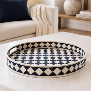 May include: A round serving tray featuring a high-contrast navy blue and cream diamond pattern across its interior and exterior walls. The tray is constructed with a smooth finish and includes two integrated cutout handles on opposite sides.