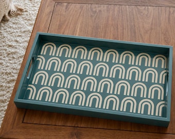 Peut inclure: Un plateau de service rectangulaire bleu sarcelle orné d'un motif répétitif d'arches couleur crème. Le plateau présente des poignées découpées intégrées sur les côtés courts et un rebord uni qui encadre le motif graphique intérieur.