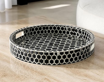 Peut inclure: Un plateau décoratif rond présentant un motif en nid d'abeille noir et blanc sur ses surfaces intérieure et extérieure. Le plateau possède un rebord surélevé avec deux poignées rectangulaires découpées intégrées pour faciliter le transport.