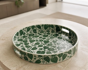 Peut inclure: Un plateau de service rond orné d'un motif continu de feuilles en forme de cœur vert foncé et de fines vignes sur fond blanc. Le plateau présente des bords surélevés avec deux poignées découpées intégrées de chaque côté pour le transport.
