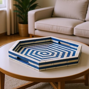 May include: A hexagonal serving tray featuring a repeating pattern of alternating blue and off-white stripes. The tray has a flat base, raised sides, and two integrated cutout handles on opposite ends, constructed with a smooth, tiled finish.