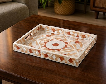 Peut inclure: Un plateau de service rectangulaire présentant un motif géométrique en mosaïque dans des tons terre cuite, crème et blanc. Le plateau possède des bords surélevés avec des poignées découpées et une base ornée d'un motif central en étoile.