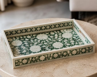 Peut inclure: Un plateau de service rectangulaire présentant un fond vert profond avec un motif floral blanc incrusté complexe. Le plateau possède des bords surélevés avec des poignées intégrées et une bordure florale blanche continue.