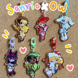 May include: Acrylic keychains featuring anime-style characters in various outfits, with the text "Sanrio x Ow" above. Each keychain has a different character design, with colorful accents and attached metal clasps for easy attachment to bags or keys.