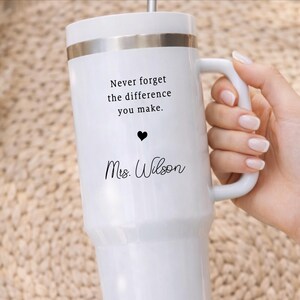 May include: White insulated tumbler with a silver rim and handle. The tumbler has the text "Never forget the difference you make." with a heart and "Mrs. Wilson" in black script. A thoughtful gift for a teacher.