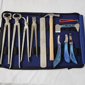 May include: A collection of farrier tools, including nippers, a rasp, a hammer, and hoof knives, arranged in a blue tool case. The tools are made of metal and wood, and are used for trimming and shaping horse hooves.