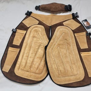 May include: A brown and tan leather riding chaps set with a matching belt. The chaps have reinforced knee pads, pockets, and adjustable buckles. The set is designed for equestrian activities and provides protection and comfort.