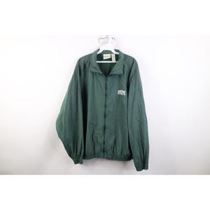 Puede incluir: Chaqueta verde oscuro con cremallera y la palabra "STATE" en letras blancas en el pecho. La chaqueta tiene cuello y está colgada de una percha blanca sobre un fondo blanco. La chaqueta es de un material ligero.