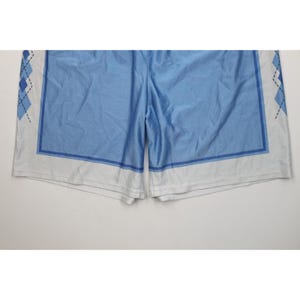 May include: Light blue athletic shorts featuring a white hem and side panels decorated with a dark blue argyle diamond pattern. The shorts have a solid light blue center section framed by a dark blue rectangular border on each leg panel.