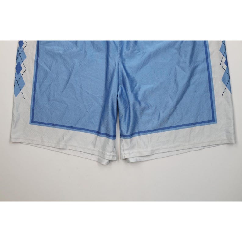 May include: Light blue athletic shorts featuring a white hem and side panels decorated with a dark blue argyle diamond pattern. The shorts have a solid light blue center section framed by a dark blue rectangular border on each leg panel.
