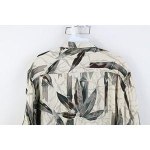 Op de afbeelding: Een cr&egrave;me overhemd met knopen en een bamboebladpatroon in groen, bruin en grijs. Het overhemd hangt aan een witte hanger.