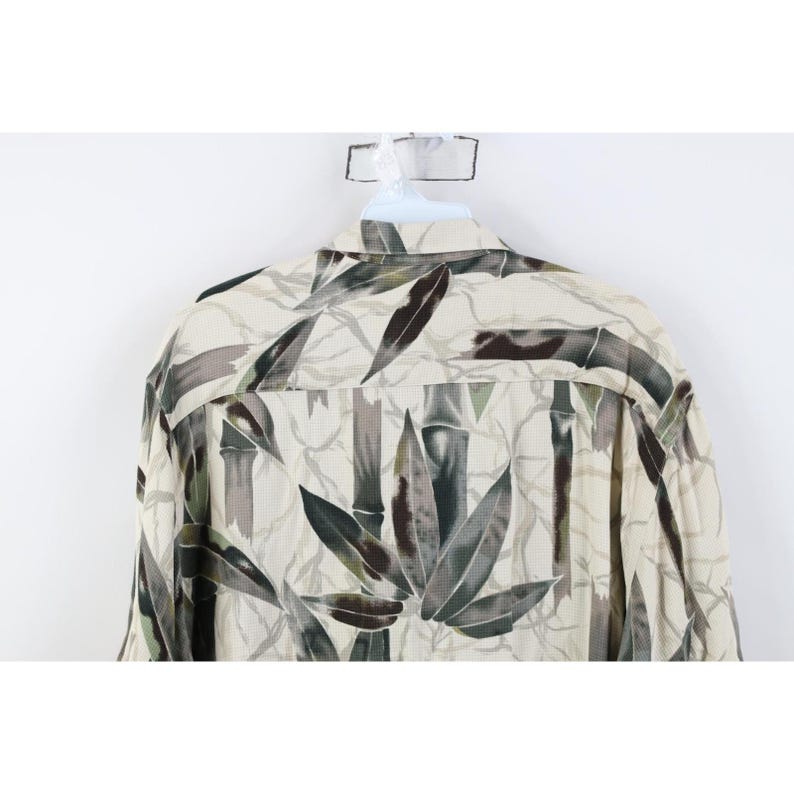 Op de afbeelding: Een cr&egrave;me overhemd met knopen en een bamboebladpatroon in groen, bruin en grijs. Het overhemd hangt aan een witte hanger.