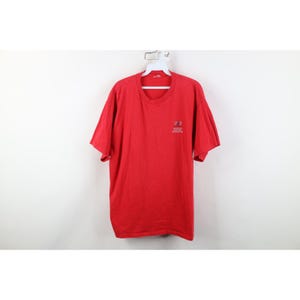 May include: A red short-sleeve t-shirt with a small logo on the upper left chest. The shirt is hanging on a white hanger against a white background. The t-shirt is made of a soft material.