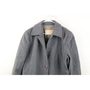 May include: A gray wool coat with a classic collar and button closure. The coat is hanging on a white hanger against a white background. The coat has a tailored fit and a simple, elegant design.