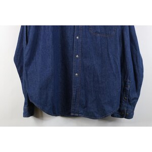 May include: A long-sleeved, dark blue denim shirt. The shirt has a button-down front, a chest pocket, and buttoned cuffs. The fabric appears to be a medium-weight denim.