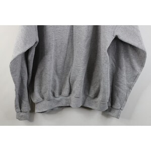 May include: A heather gray long-sleeve sweatshirt featuring a crew neckline, ribbed cuffs at the wrists, and a ribbed hemline. The garment is constructed from a soft, fleeced fabric with a consistent light gray tone throughout the entire piece.