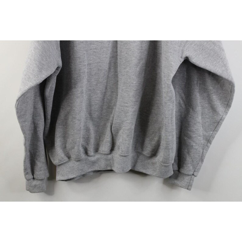 May include: A heather gray long-sleeve sweatshirt featuring a crew neckline, ribbed cuffs at the wrists, and a ribbed hemline. The garment is constructed from a soft, fleeced fabric with a consistent light gray tone throughout the entire piece.