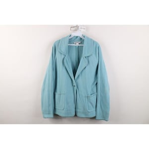 May include: A light blue blazer with a wide collar, a single front button closure, and two patch pockets. The garment features long sleeves and a textured fabric construction. A white plastic hanger is attached to the collar area.