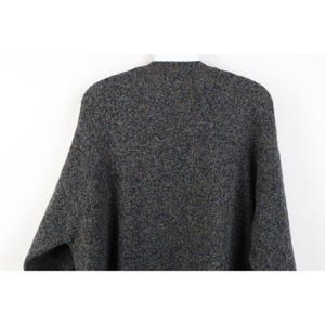May include: A gray, textured sweater with a crew neck. The sweater has a speckled pattern with flecks of blue, brown, and yellow. The sleeves are long and the material appears to be a thick knit.