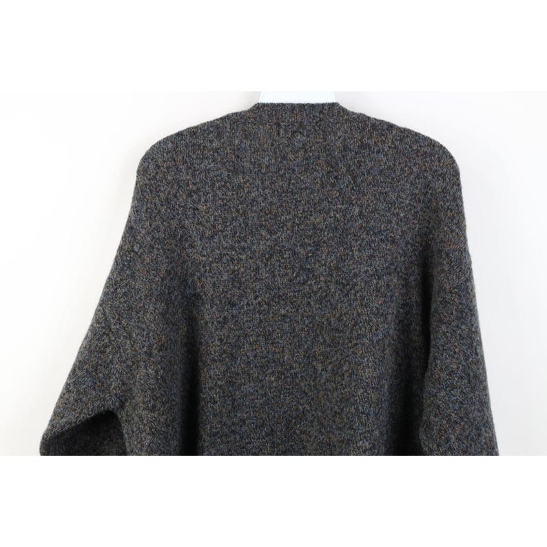 May include: A gray, textured sweater with a crew neck. The sweater has a speckled pattern with flecks of blue, brown, and yellow. The sleeves are long and the material appears to be a thick knit.