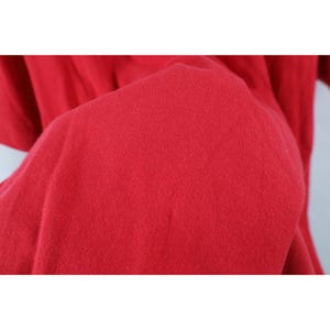 May include: Close-up of a vibrant red fabric, likely a piece of clothing. The material appears soft and slightly textured, with subtle variations in the color. The image focuses on the texture and color of the textile.