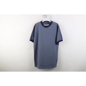 May include: A short-sleeved ringer t-shirt in a heathered blue fabric with a solid dark navy blue trim around the crew neckline and sleeve cuffs. The shirt is displayed on a white plastic hanger against a plain, neutral background.