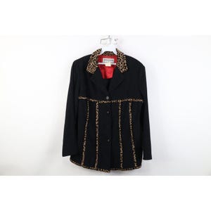 May include: A black blazer with leopard print accents on the collar and down the front. The blazer has a red lining and a button closure. The garment is hanging on a white hanger.