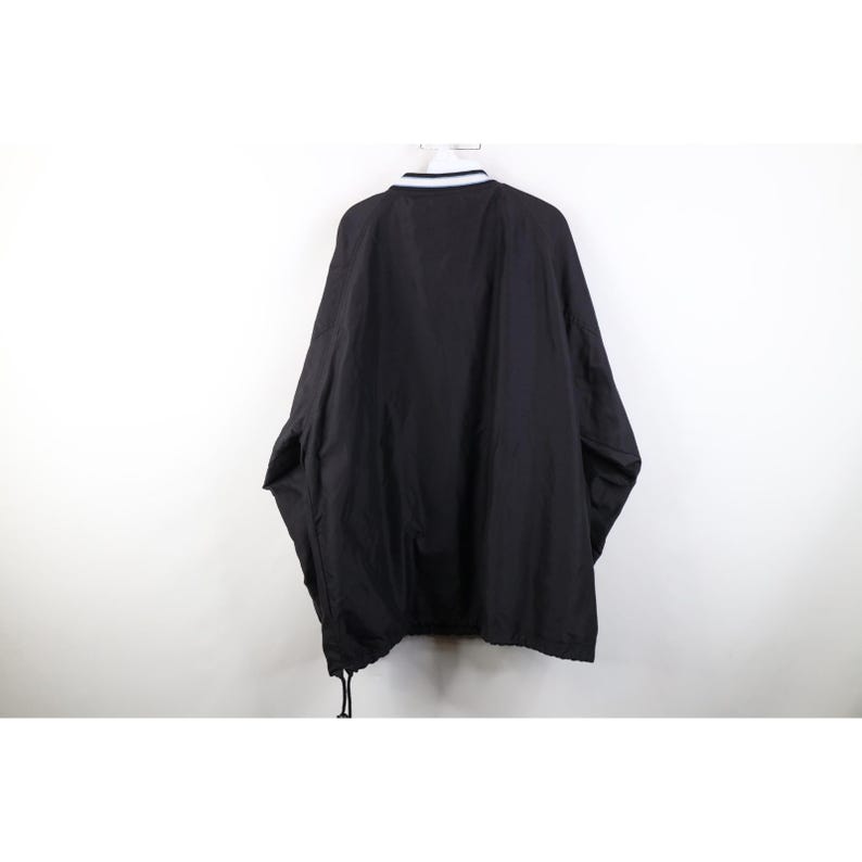 May include: Black jacket with a white and navy blue striped collar. The jacket has a drawstring at the bottom and is hanging against a white background. The jacket is a solid black color.