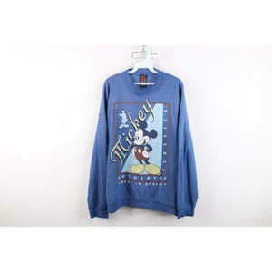Op de afbeelding: Een blauw sweatshirt met lange mouwen en een afbeelding van Mickey Mouse. Het ontwerp bevat de tekst "Mickey Classics" in gestileerd schrift, "Authentic" in blokletters en "Finest in Quality" gedrukt binnen een rechthoekige rand.
