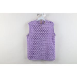 Puede incluir: Un chaleco de punto sin mangas en color lavanda con un patrón repetitivo de hojas en todo el cuerpo. La prenda tiene un cuello redondo y un dobladillo acanalado, con una percha de plástico blanca visible en la parte superior con la etiqueta R1134.
