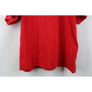 May include: A solid red t-shirt, the fabric appearing soft and slightly textured. The short sleeves and the body of the shirt are visible, with the garment hanging against a plain background. The shirt is a vibrant, saturated red.