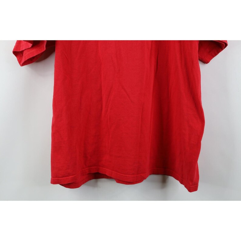May include: A solid red t-shirt, the fabric appearing soft and slightly textured. The short sleeves and the body of the shirt are visible, with the garment hanging against a plain background. The shirt is a vibrant, saturated red.