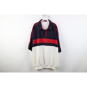 Könnte beinhalten: Ein kurzärmeliges Poloshirt in Marineblau, Rot und Weiß. Das Shirt hat einen marineblauen Kragen und Ärmel mit roten Streifen, einen roten horizontalen Streifen über der Brust und einen weißen unteren Bereich. Es hängt an einem weißen Kleiderbügel.