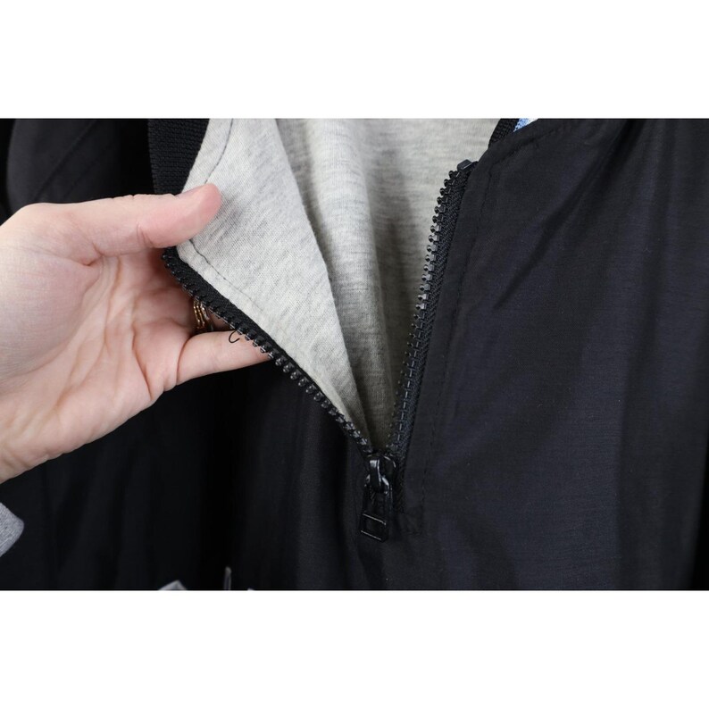 May include: Black jacket with a full zipper, revealing a gray interior lining. The jacket's zipper is black and runs down the center. The jacket is made of a smooth, possibly nylon, material.