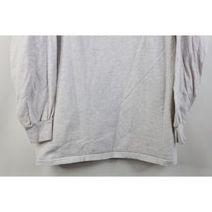 Op de afbeelding: Een lichtgrijs shirt met lange mouwen. Het shirt heeft een ronde hals en geribde manchetten. De stof lijkt een zacht, gebreid materiaal te zijn. De mouwen zijn lang en het shirt is effen van kleur.