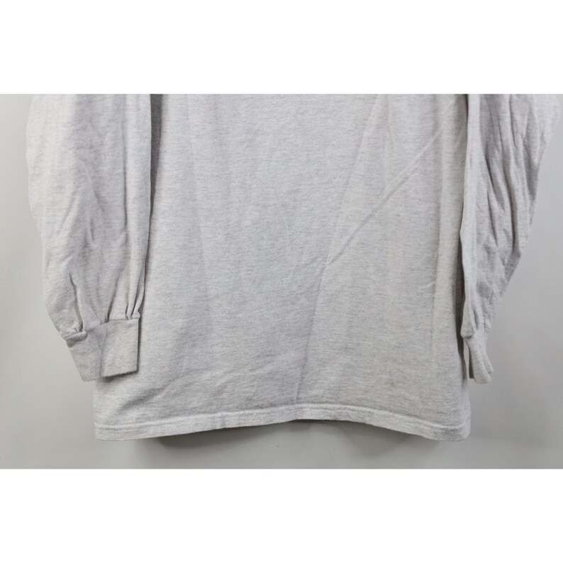 Op de afbeelding: Een lichtgrijs shirt met lange mouwen. Het shirt heeft een ronde hals en geribde manchetten. De stof lijkt een zacht, gebreid materiaal te zijn. De mouwen zijn lang en het shirt is effen van kleur.