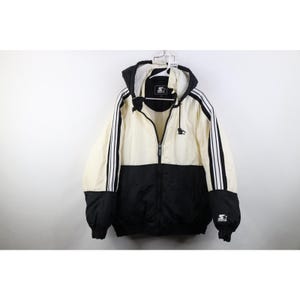 May include: A hooded jacket in cream and black, featuring a full zipper and the Starter logo. The jacket has black stripes down the sleeves and a black lower section. The Starter logo is also on the sleeve.