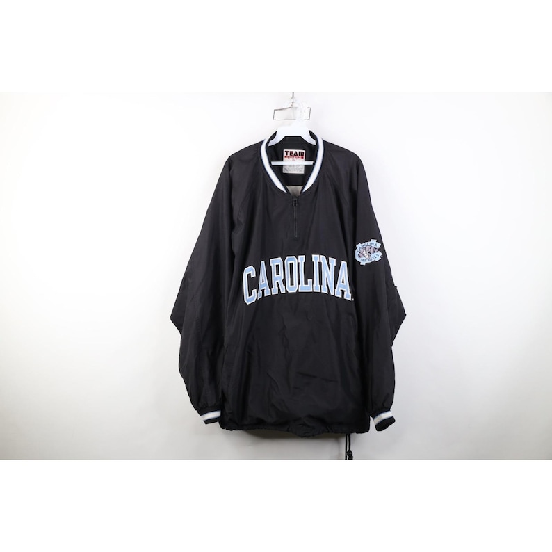 May include: Black pullover jacket with the word "CAROLINA" in light blue across the chest. The jacket has a white collar and cuffs, and a small logo on the right sleeve. The jacket is hanging on a white hanger.