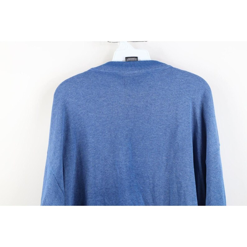Op de afbeelding: Een effen blauwe trui met ronde hals en een gem&ecirc;leerde textuur. Het kledingstuk heeft een geribbelde halslijn en wordt getoond op een witte plastic hanger. De stof heeft een consistente medium blauwe tint met een zachte gebreide uitstraling.