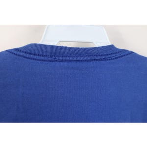 May include: Close-up of a royal blue crew neck t-shirt. The neckline is ribbed and has a double-stitched seam. The shirt is hanging on a white plastic hanger. The fabric appears to be a soft, knit material.