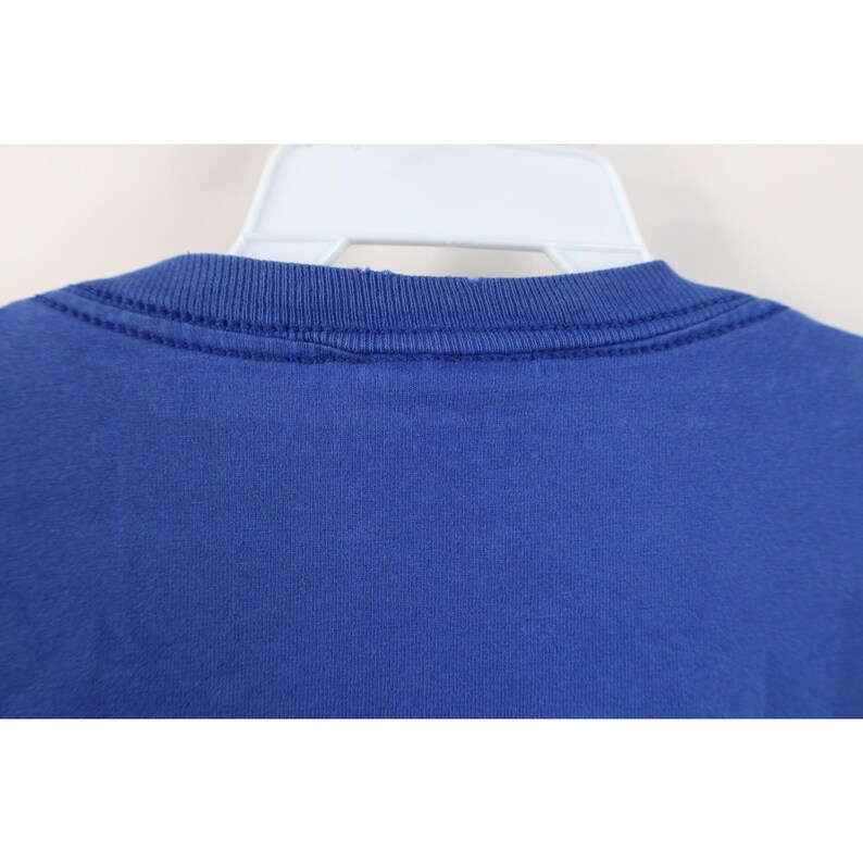 May include: Close-up of a royal blue crew neck t-shirt. The neckline is ribbed and has a double-stitched seam. The shirt is hanging on a white plastic hanger. The fabric appears to be a soft, knit material.