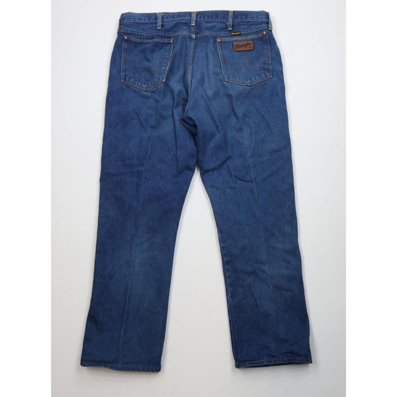 Op de afbeelding: Donkerblauwe spijkerbroek met een klassiek ontwerp met vijf zakken. De jeans heeft een bruine leren patch met de merknaam. De achterzakken hebben een klassiek stikselontwerp. De jeans liggen plat op een witte ondergrond.