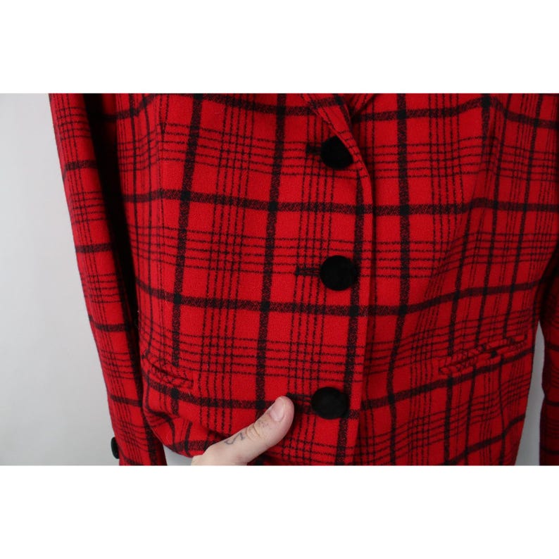 Peut inclure: Un blazer &agrave; carreaux rouges et noirs avec des boutons noirs. La veste pr&eacute;sente un motif &agrave; carreaux classique et une coupe ajust&eacute;e. Les boutons sont ronds et noirs, et le blazer a un col crant&eacute;.