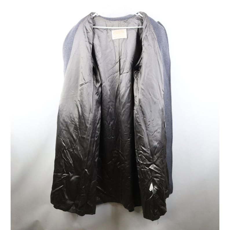 May include: A gray wool coat with a dark gray satin lining. The coat is open, revealing the interior lining and a small label. The coat is hanging on a white hanger against a white background.