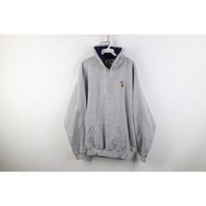 May include: A heather gray pullover hoodie featuring a small embroidered Mickey Mouse character on the left chest. The garment includes a dark navy blue inner hood lining, a front kangaroo pocket, long sleeves, and a drawstring hood closure.