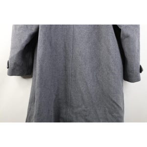 May include: A gray wool coat with long sleeves and a button detail on the cuffs. The coat has a classic, tailored design and a subtle texture. The coat is a neutral color, suitable for various outfits.