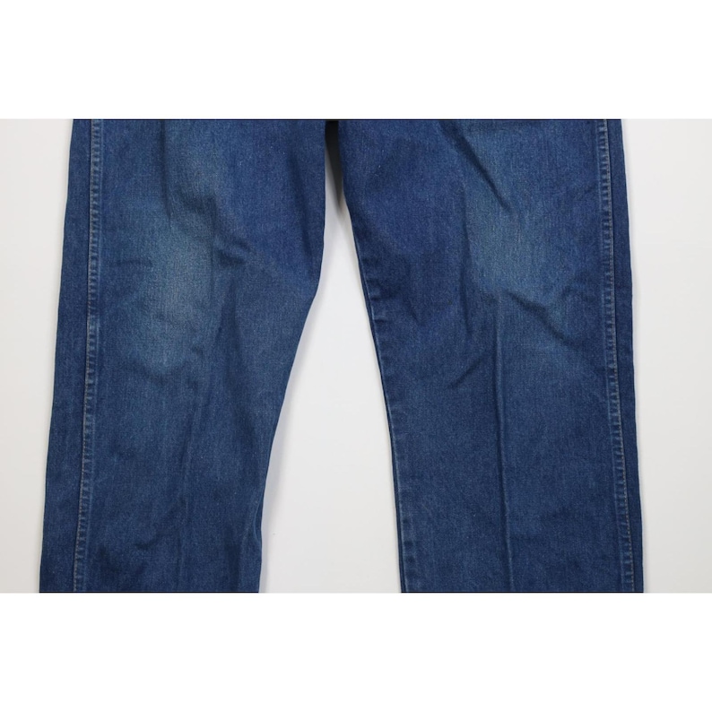 Op de afbeelding: Close-up van een blauwe spijkerbroek. De jeans heeft een klassiek ontwerp met vijf zakken, met een rechte pijp. De denim heeft een medium wassing met wat vervaging en slijtage.